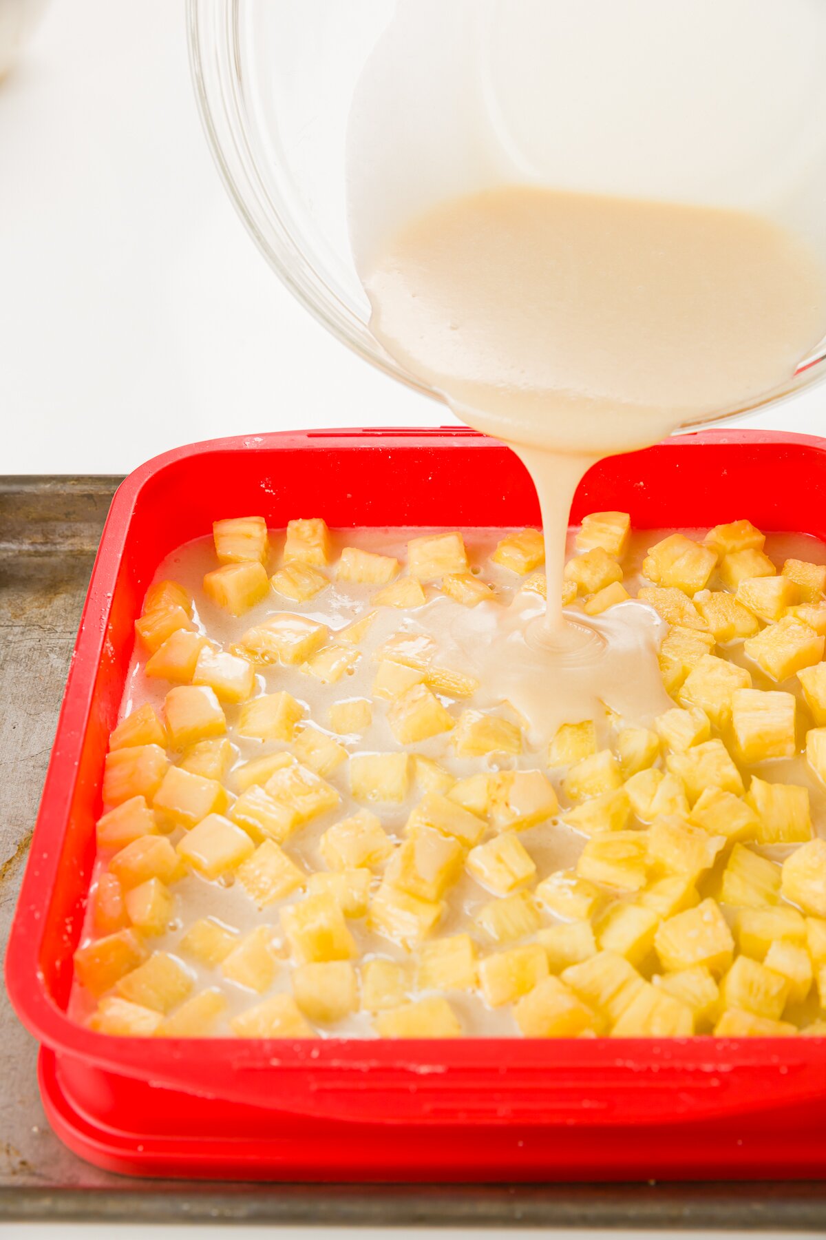 Pour batter from a glass bowl over baking dish with crust and pineapple