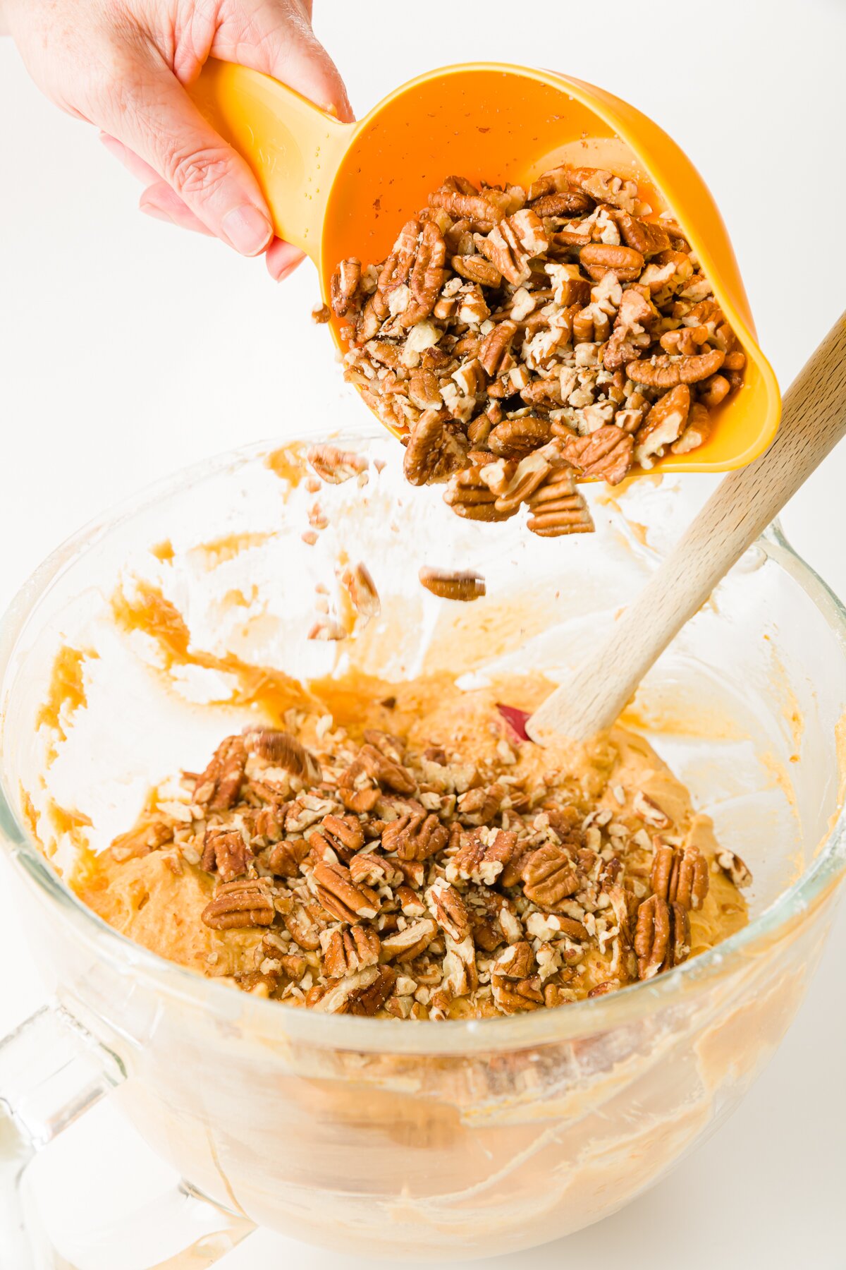 Pouring pecans into a glass mixing bowl filled with batter