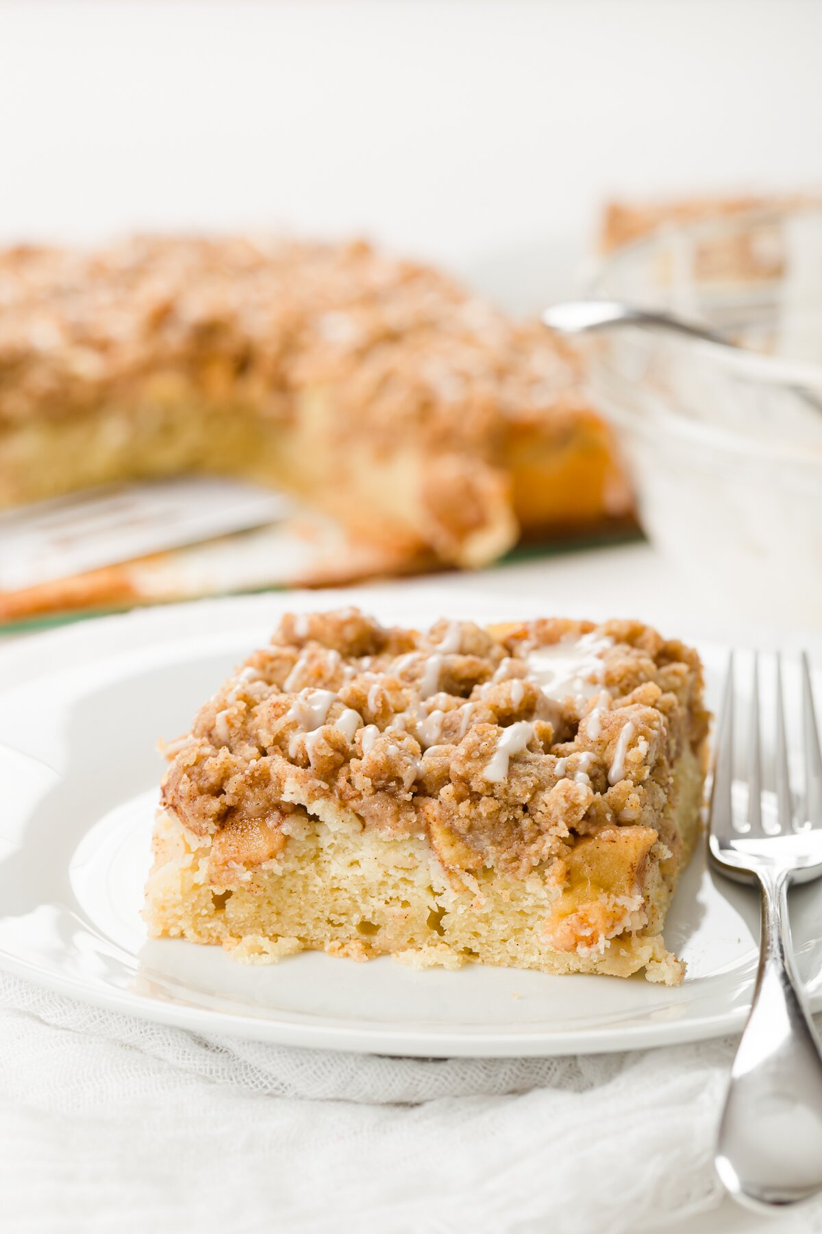 Slice of apple crumb cake with the cake in the background