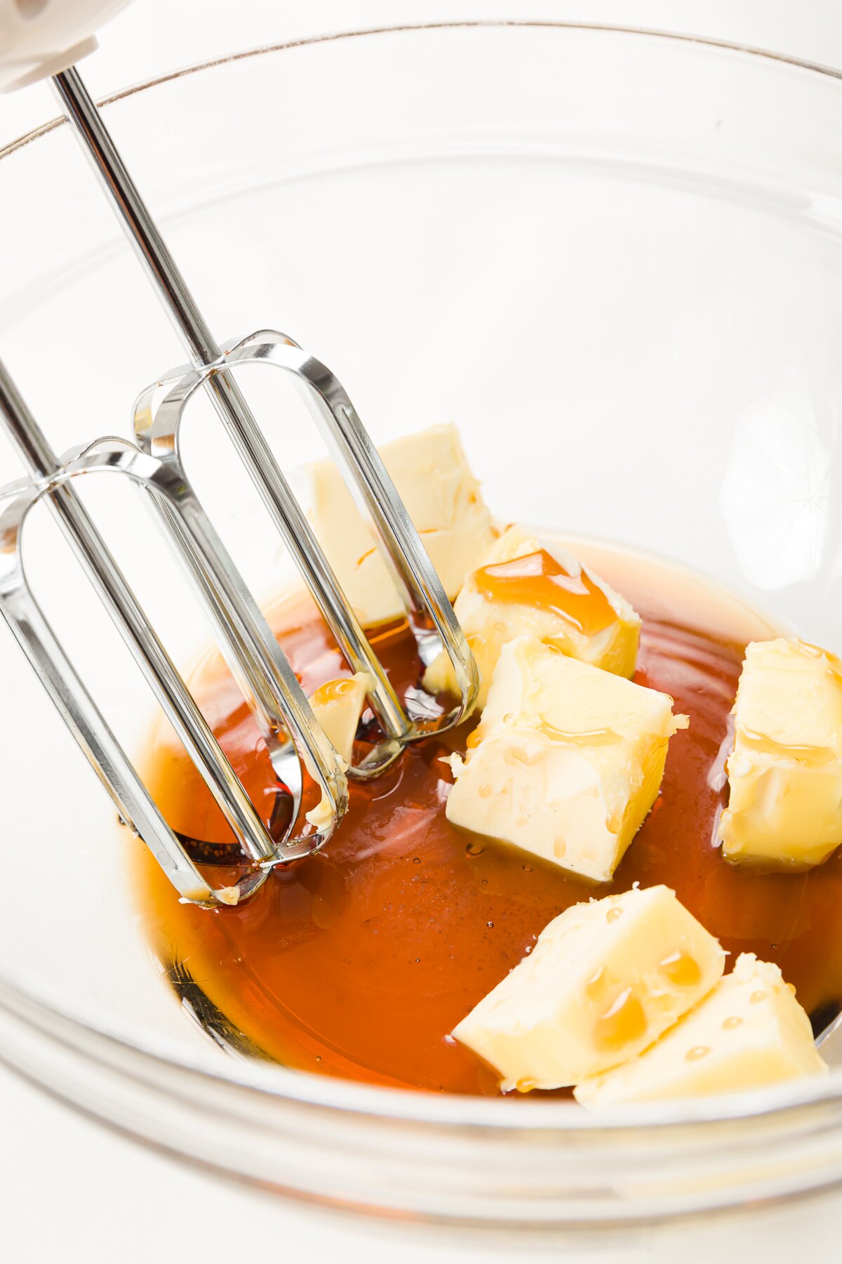 Maple and chunks of butter in a glass bowl with hand mixer blades