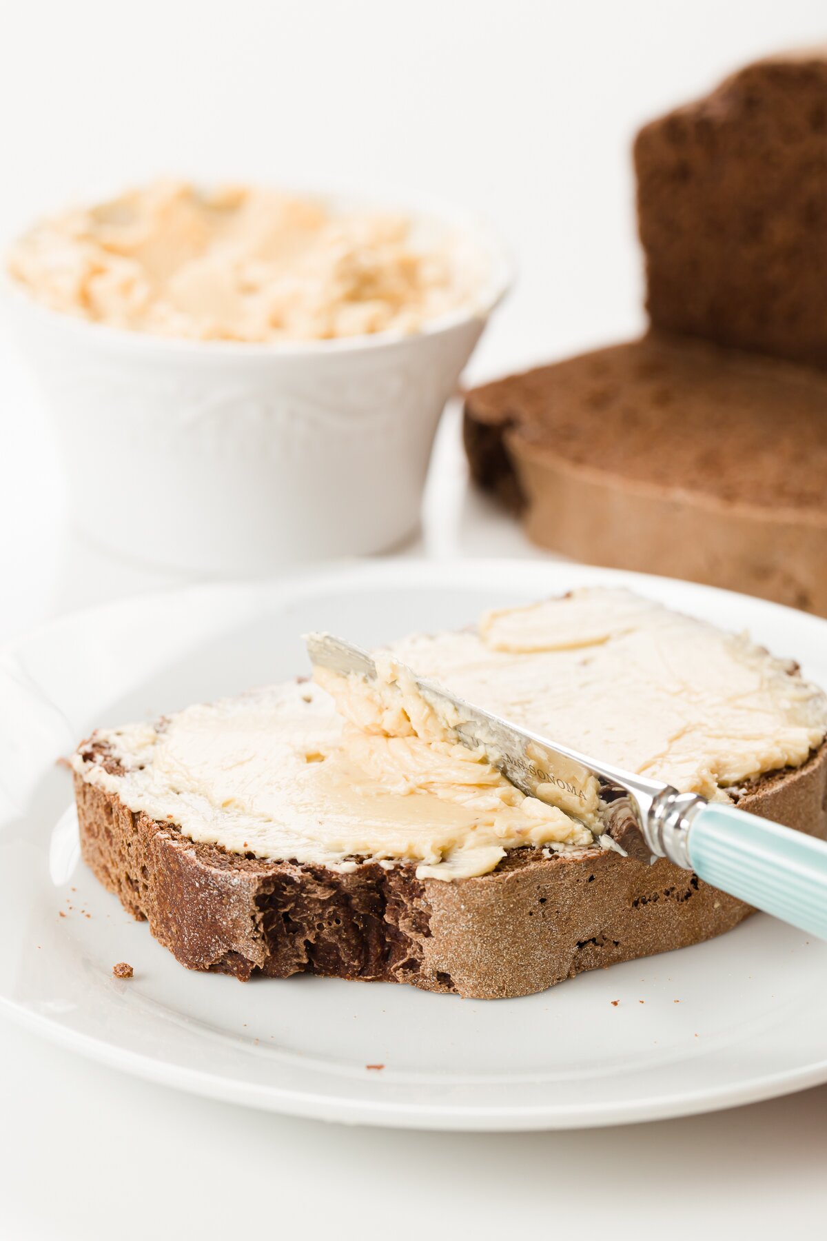 Maple butter being spread on a slice of bread with a ramekin of maple butter in the background