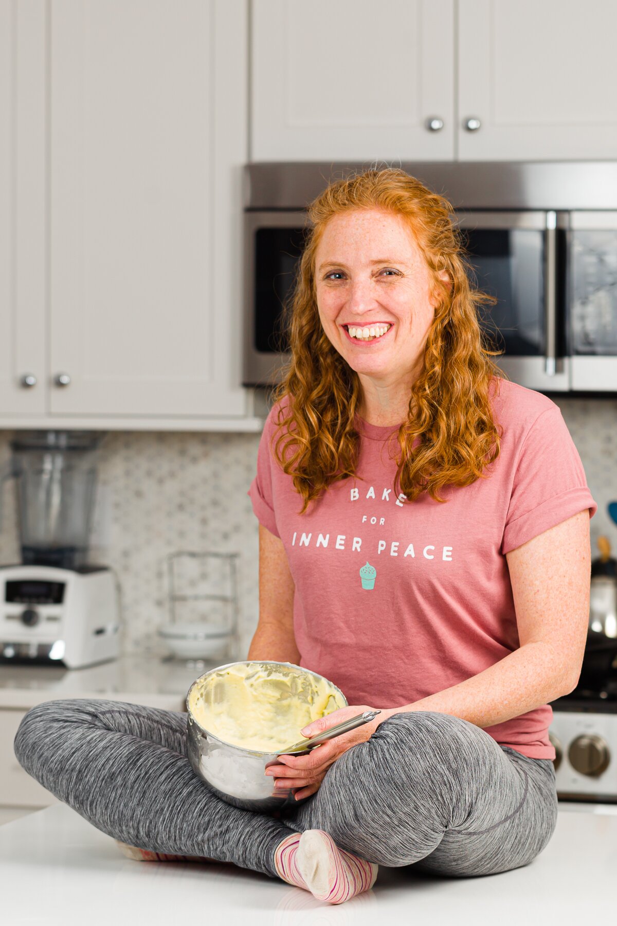 Stef sitting on the kitchen island with a mixing bowl full of batter