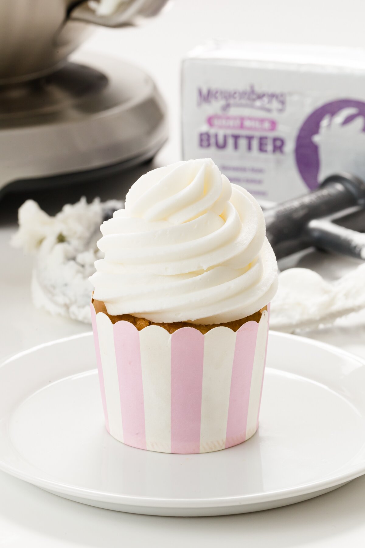 Cupcake in a pink and white stripe wrapper with a package of goat butter in the background