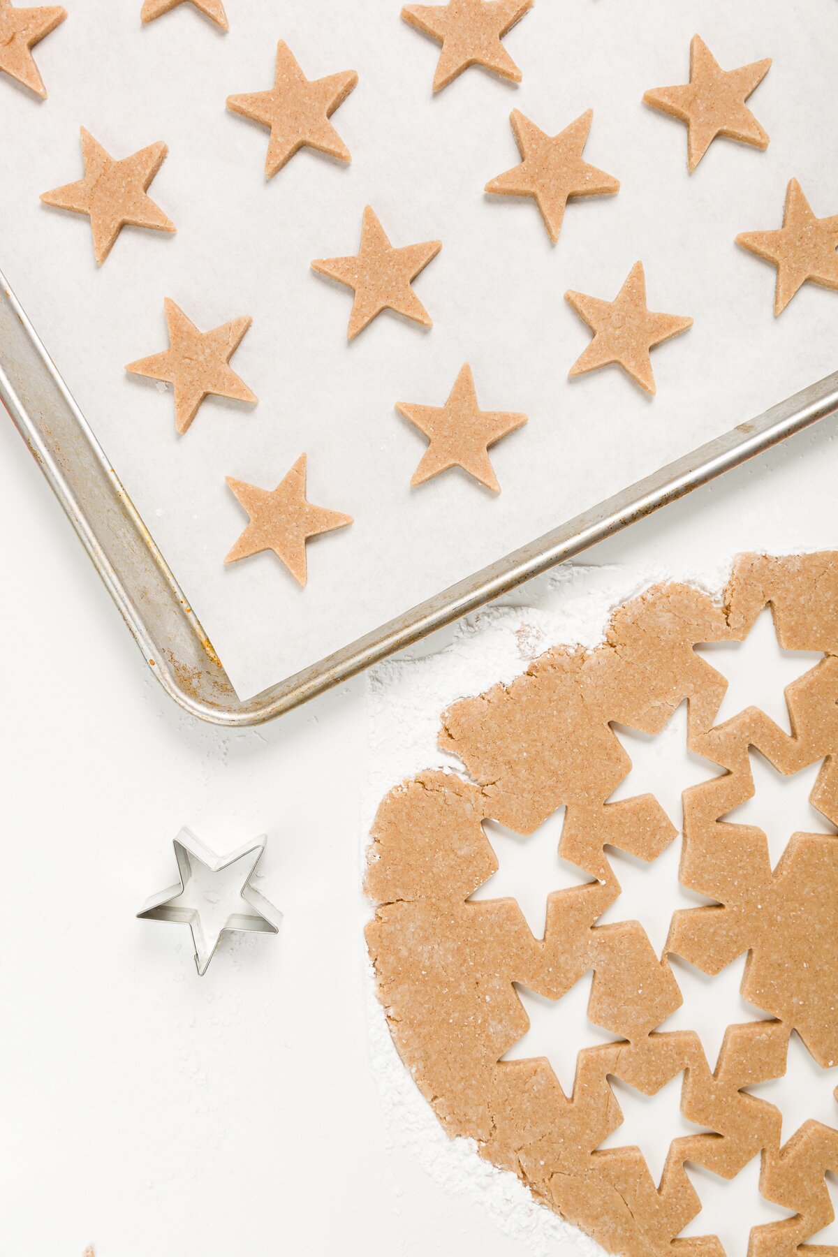 Rolled out cookie dough with stars cut out and cut out stars above it on a parchment-lined cookie sheet