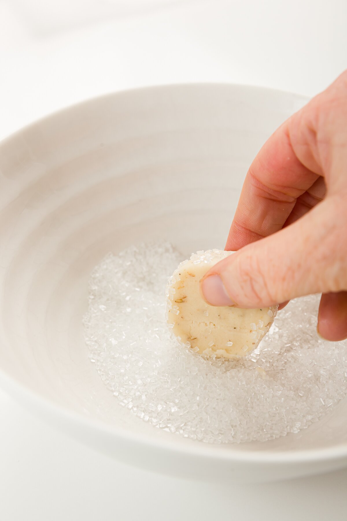 Rolling cookie dough in sugar in a white bowl