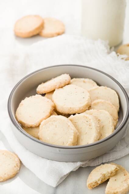 Lavender shortbread in a grey bowl with cookies and milk around it