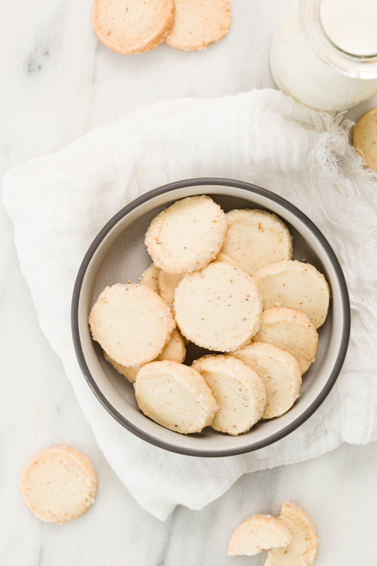 Top down view of lavender shortbread cookies in a bowl with cookies and milk around it