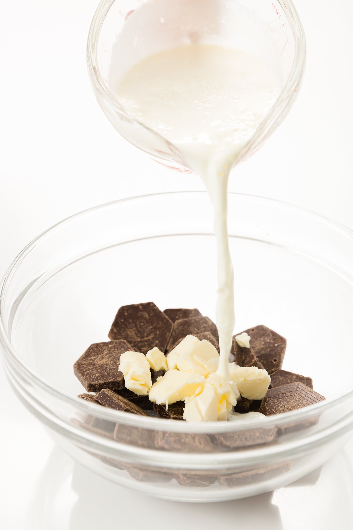 Pouring cream over chocolate and butter in a glass bowl