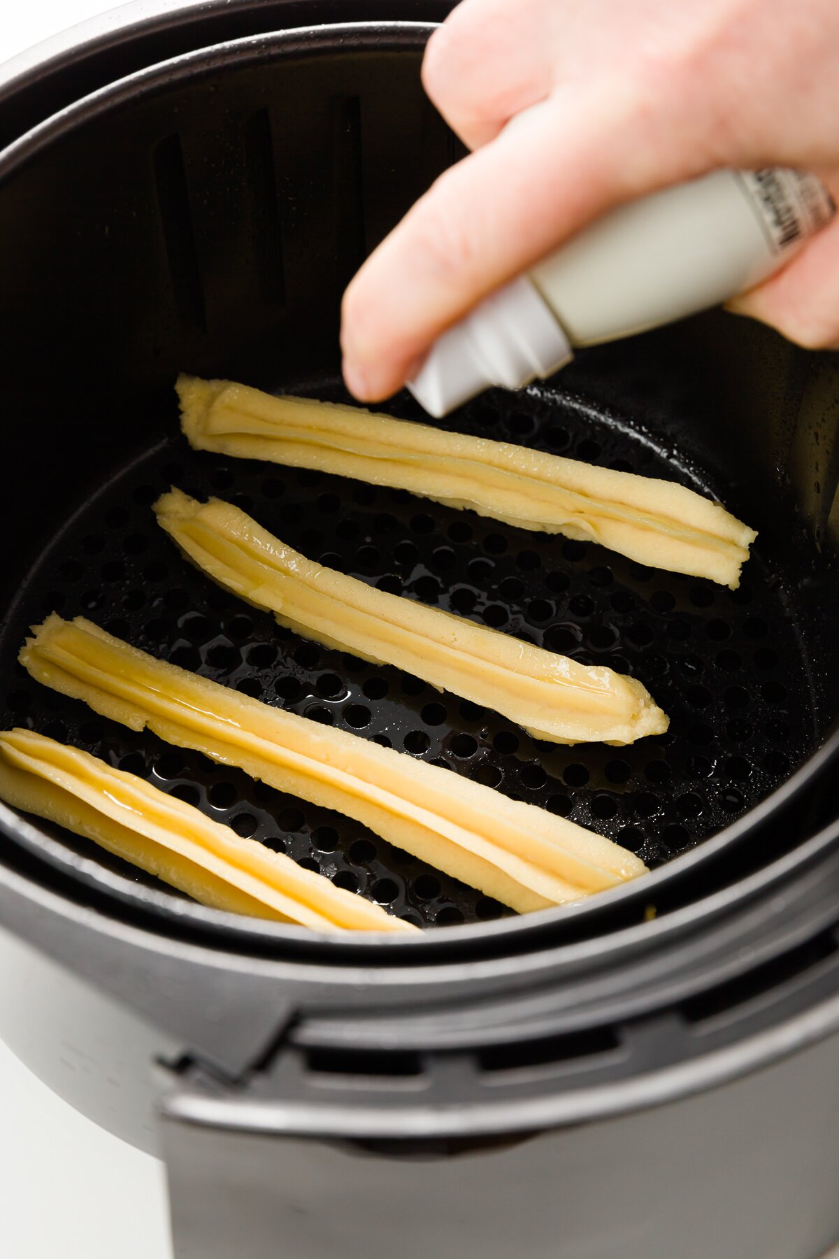 Spraying churros with cooking spray in the basket of an air fryer