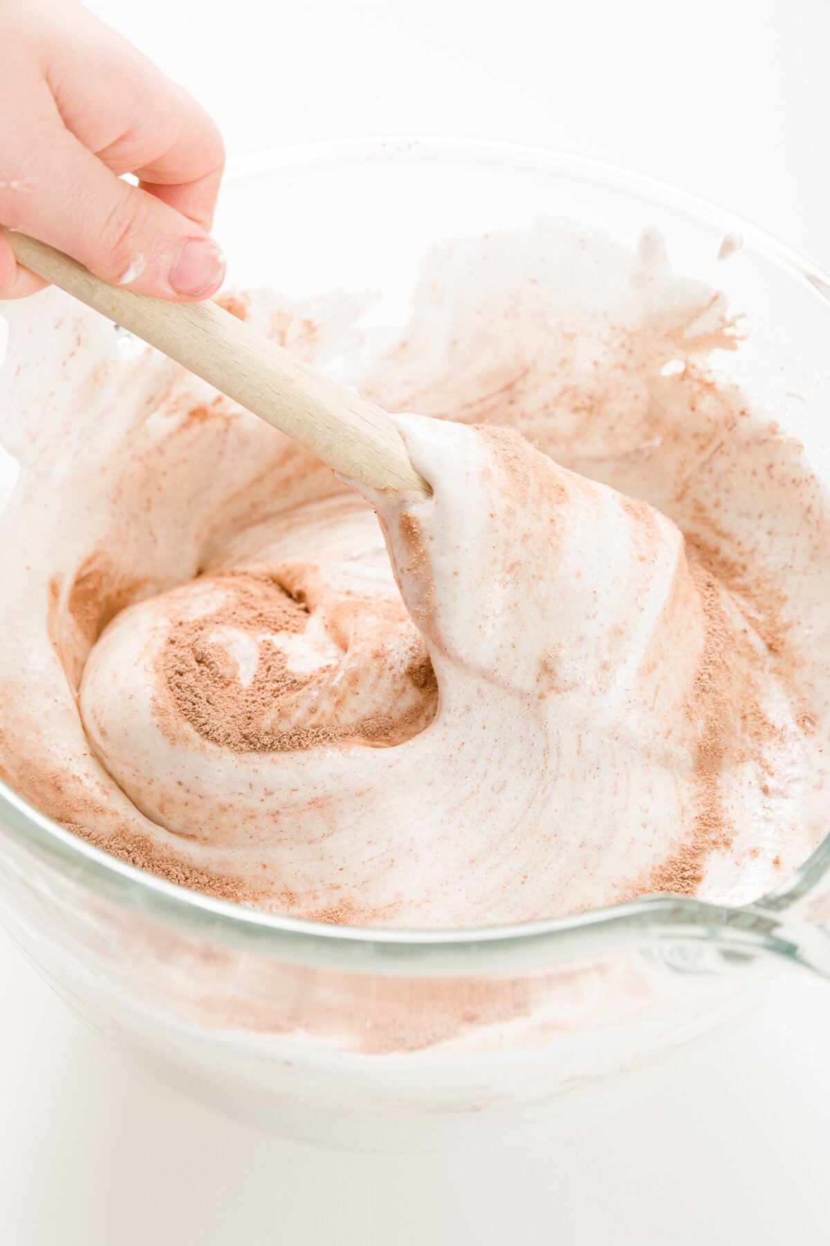 Folding in cocoa powder and other dry ingredients into whipped eggs with a spatula in a glass bowl