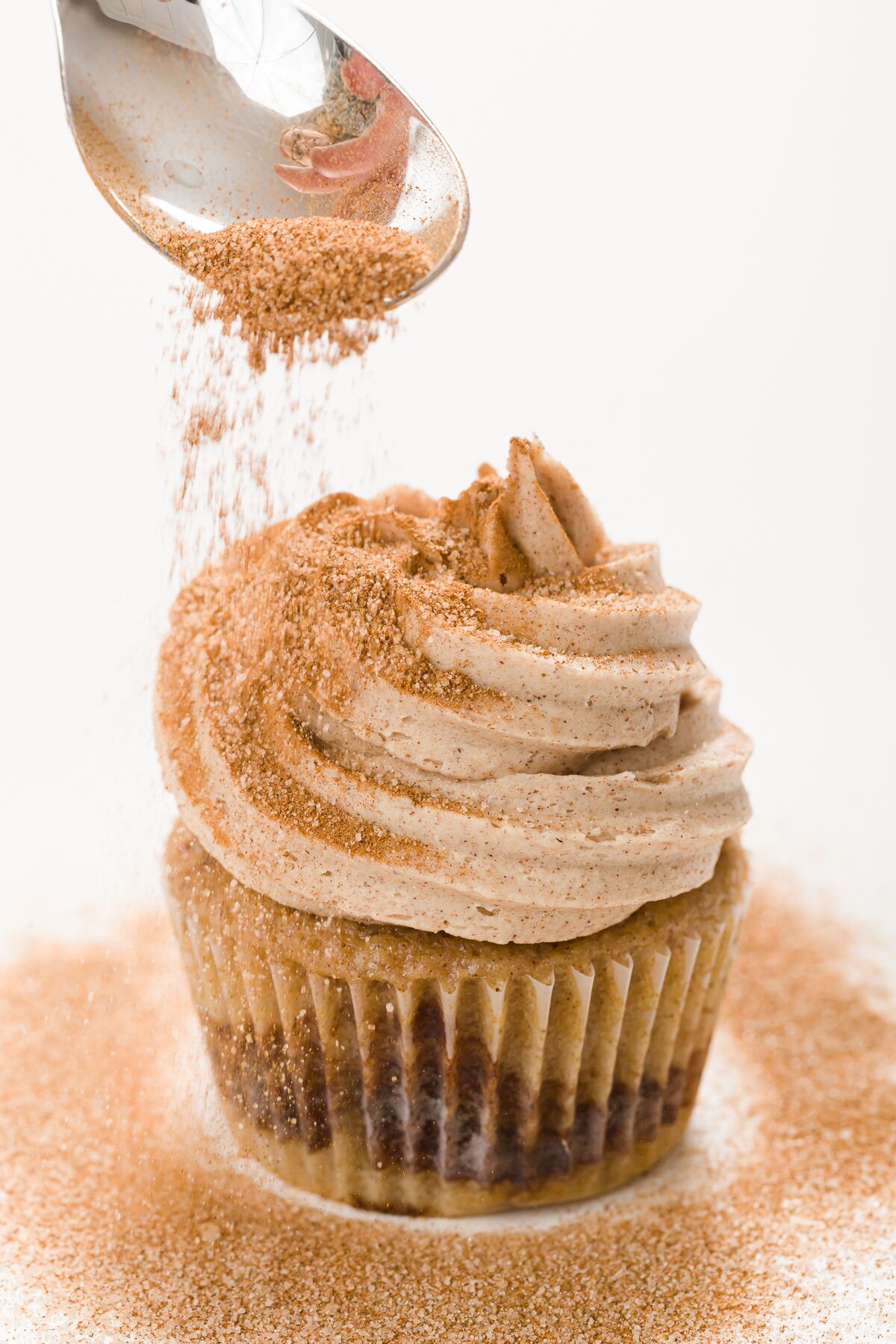 Cinnamon and Sugar being dusted over cinnamon buttercream frosting on a cupcake