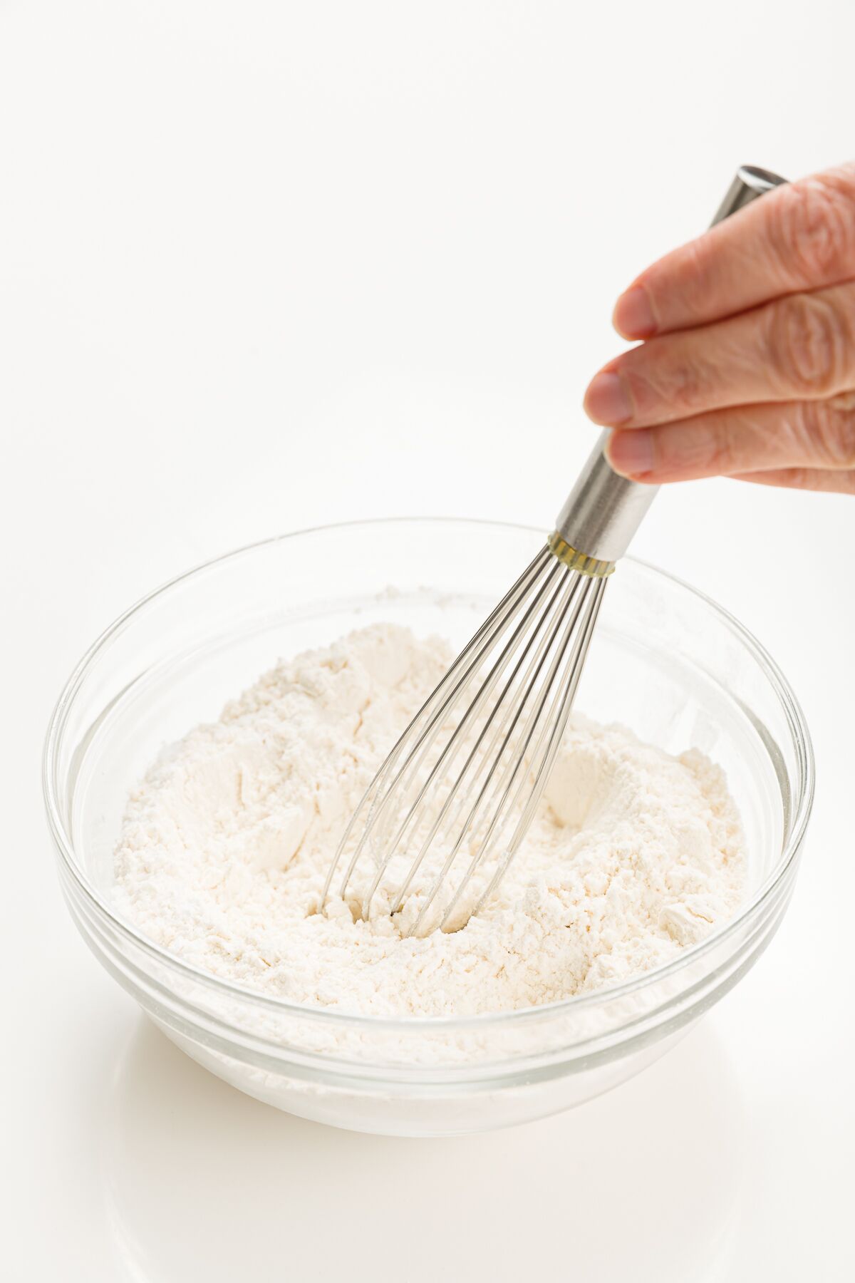 Hand holding whisk mixing up dry ingredients in a clear glass bowl
