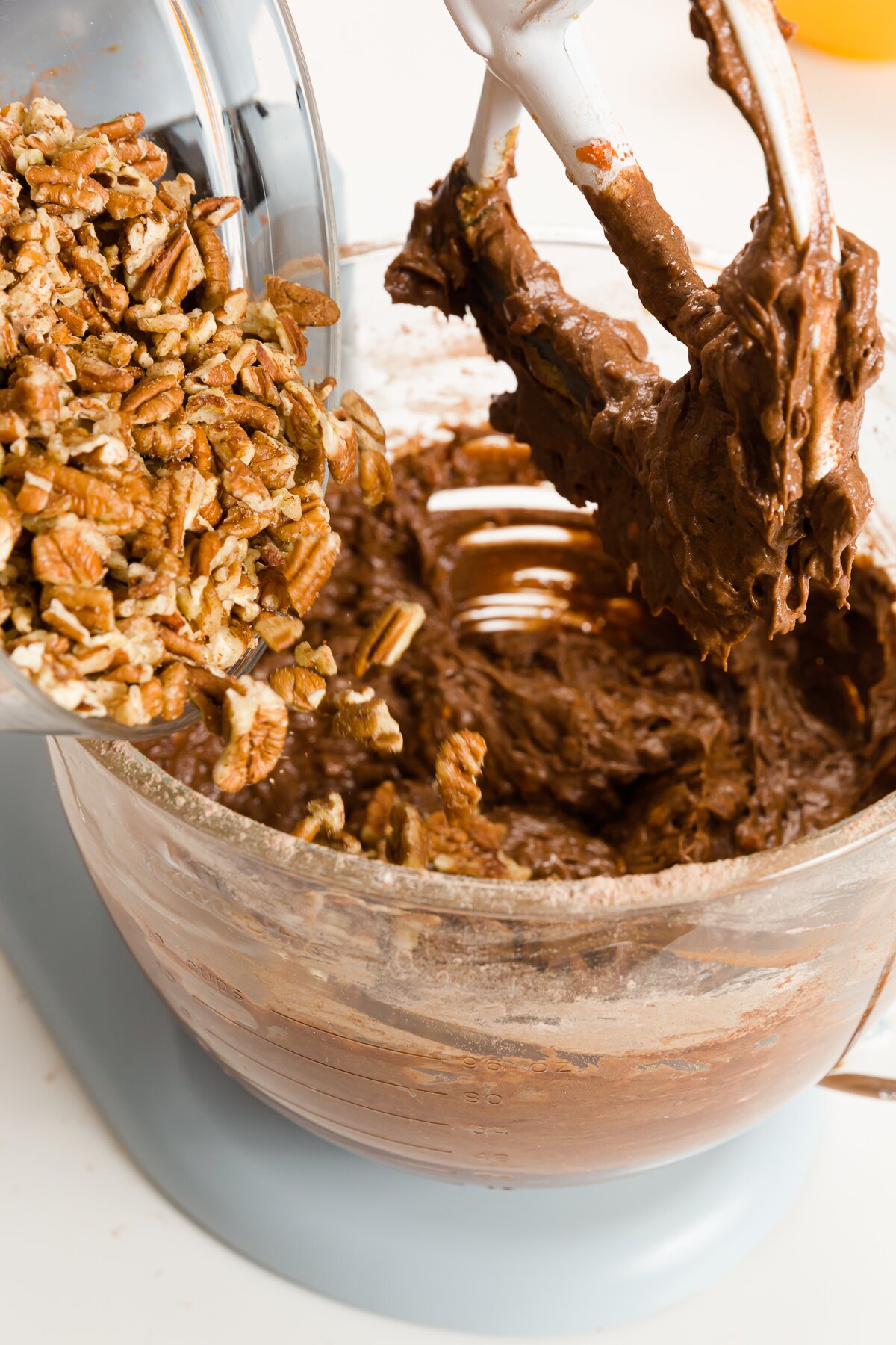 Pour chopped pecans into the bowl of a stand mixer from a glass bowl