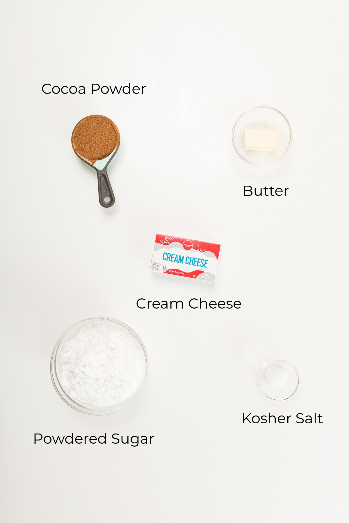 Overhead view of ingredients in chocoalte cream cheese frosting - cocoa powder, butter, cream cheese, powdered sugar, and kosher salt