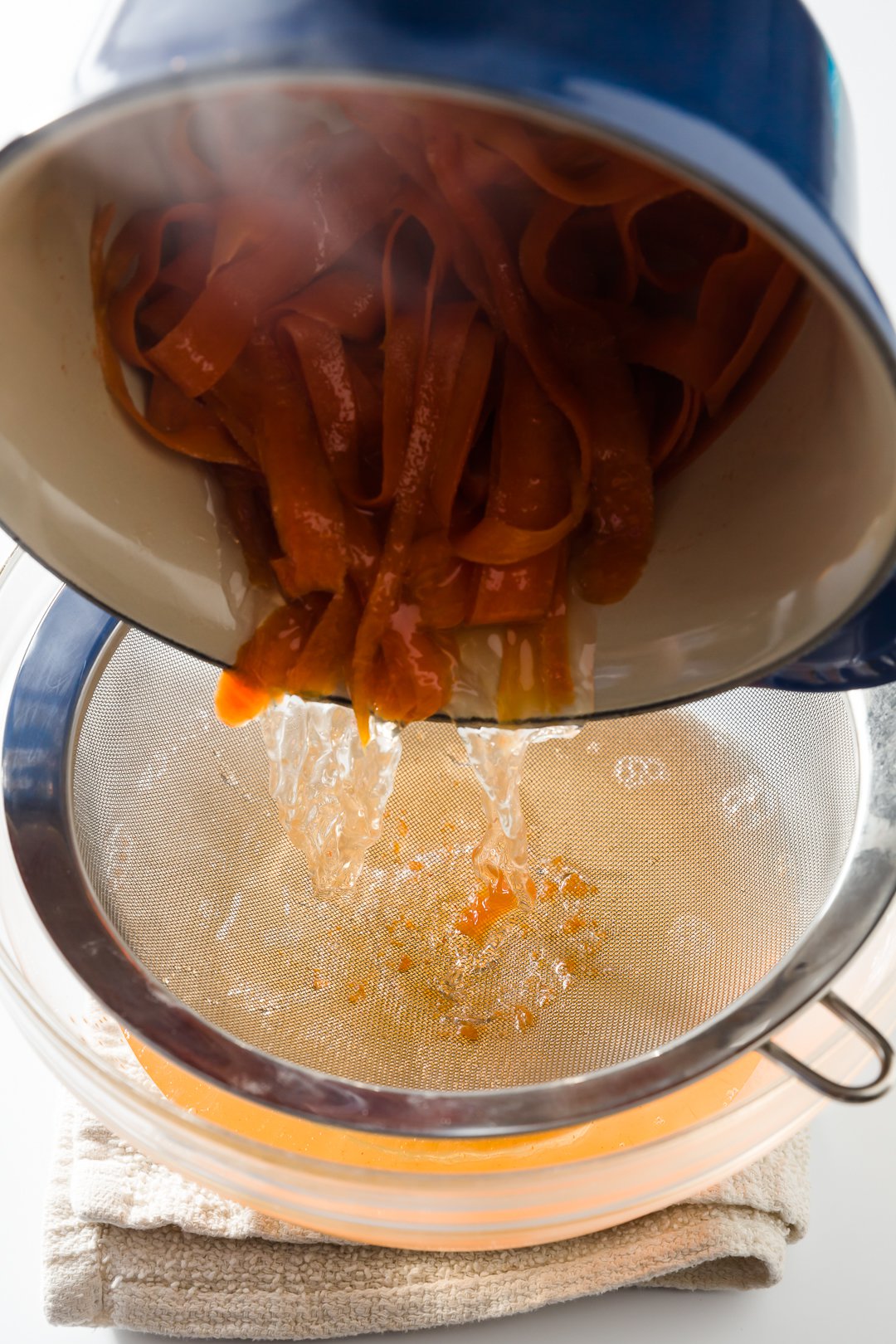 Pouring carrot ribbons into a strainer over a bowl.