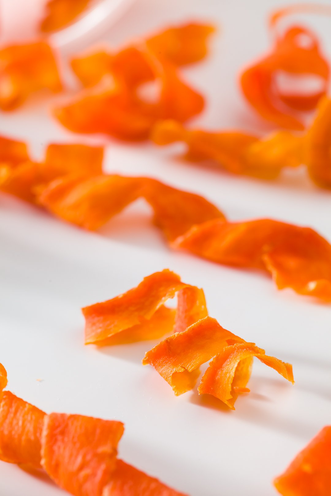 Close up of finished candied carrot curls on a parchment lined baking tray.