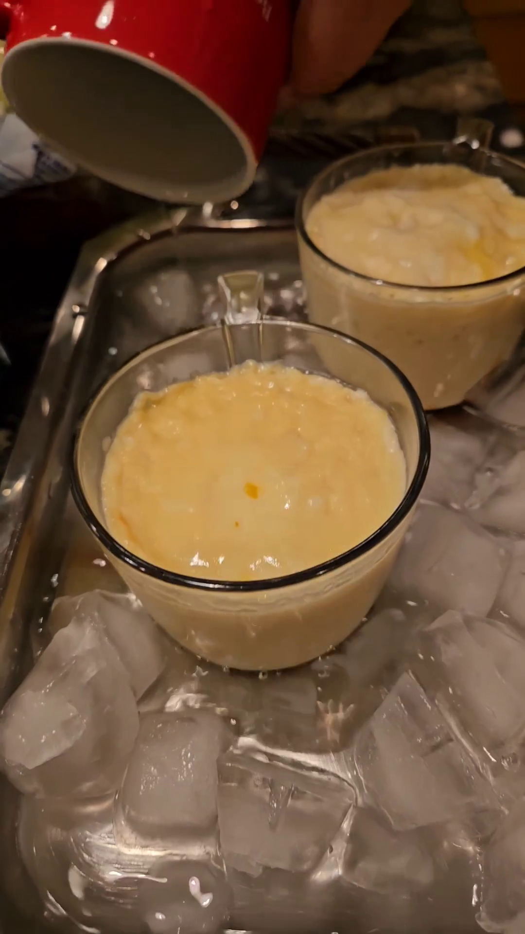 Glass cups of cooked microwave flan in an ice water bath.