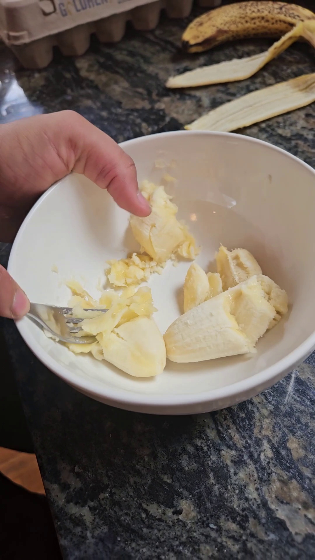 Using a fork to mash a banana in a white bowl.